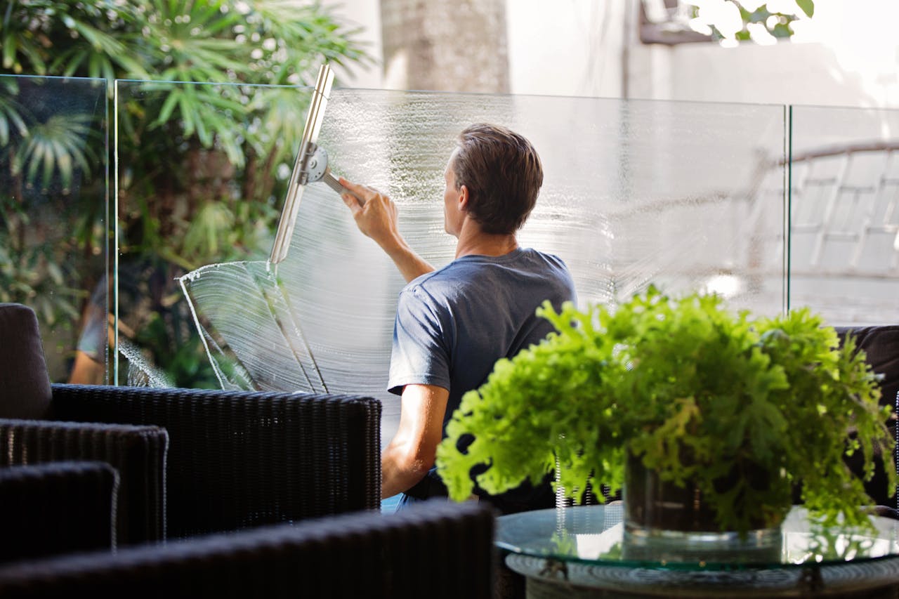 core-values A man cleaning a glass barrier outdoors with a squeegee, surrounded by greenery.